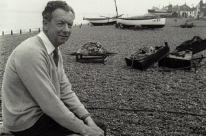 Benjamin Britten on the shingle at Aldeburgh, fishing boats behind him.