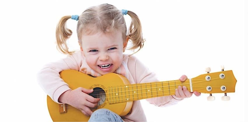 A young girl playing a yellow guitar with a big smile