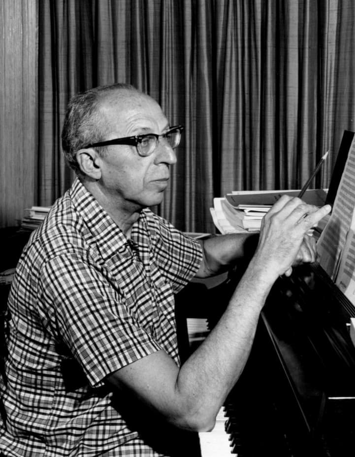 Photo of Aaron Copland composing at the piano, 1962