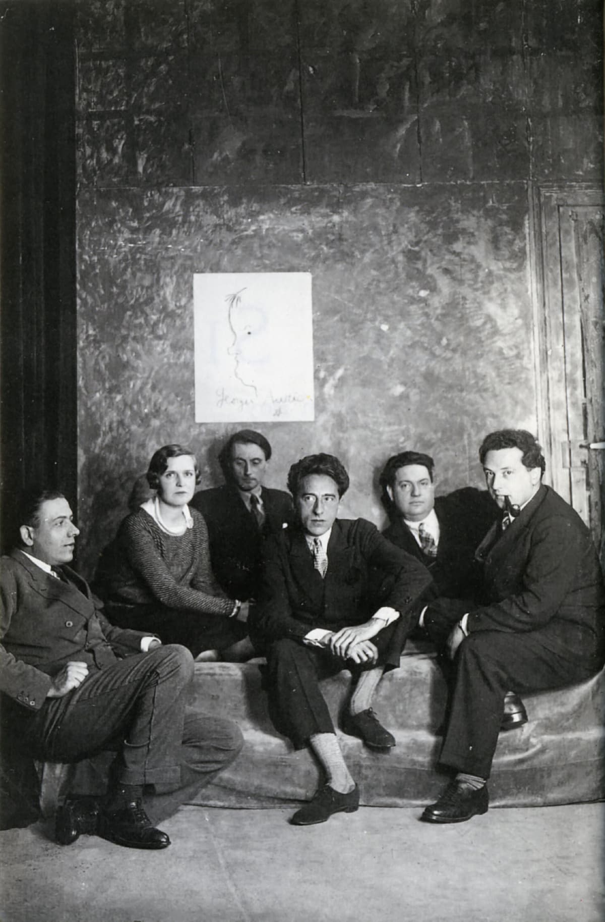 Les Six, left to right: Francis Poulenc, Germaine Taileferre, Louis Durey, Jean Cocteau, Darius Milhaud, Arthur Honegger. Sketch of Georges Auric on the wall behind them.