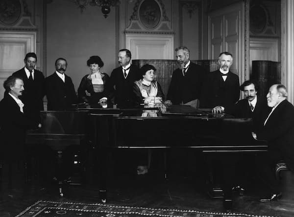 Ignacy Paderewski (left) and Camille Saint-Saëns (right) seated at a pair of pianos in a lounge at the Hôtel des Trois Couronnes in Vevey, 1913. Also in the picture are Charles Pilet (organist), Viscount de Faria (consul of Portugal), Mrs Schelling, Auguste Roussy (Swiss politician), Helena Paderewska, Mr Beaud (ambassador of France to Switzerland), Eugène Couvreu (mayor of Vevey), and Ernest Schelling (American pianist–composer)